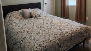 Un dormitorio con cama, puerta y ventana con cortinas.