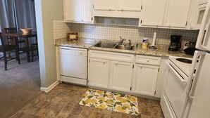 Una cocina con armarios blancos, lavavajillas, estufa y cafetera.