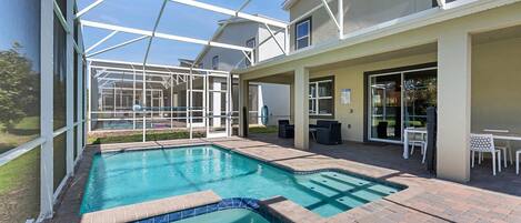 A swimming pool with a glass enclosure, patio seating, and a covered outdoor area.