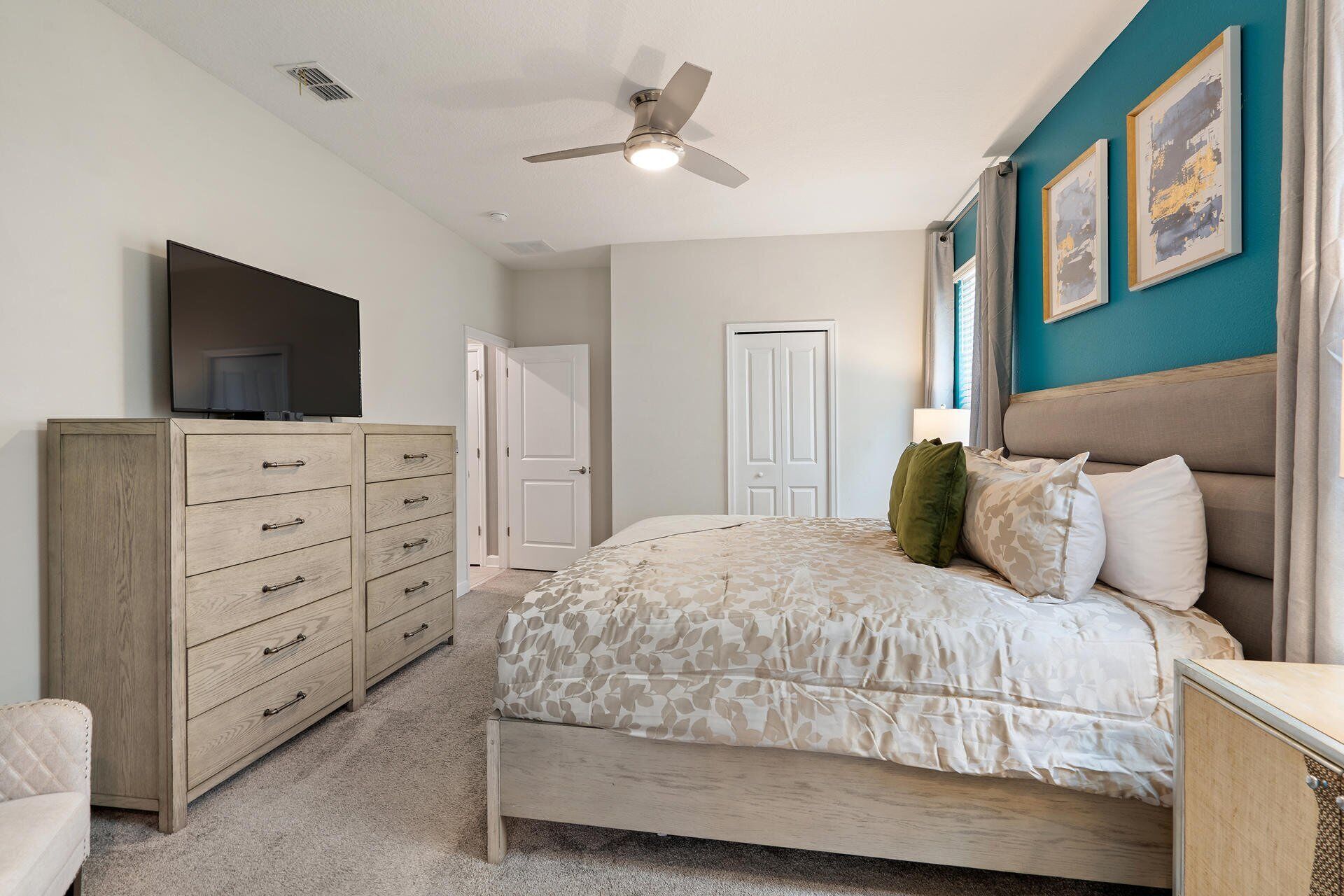 A bedroom with a bed, a dresser, a television, a ceiling fan, and a door.