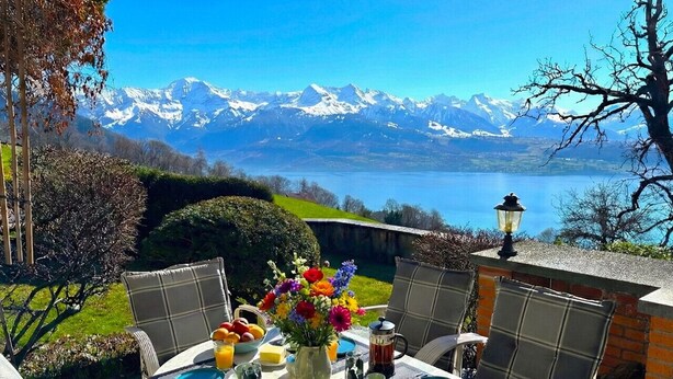 A table set for breakfast with a mountain view, including a lake and snow-capped peaks.