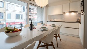 A modern kitchen with white cabinets, a dining table with chairs, and a large window offering a view of the city. - Heritage with parking by Interhome (Bredene)
