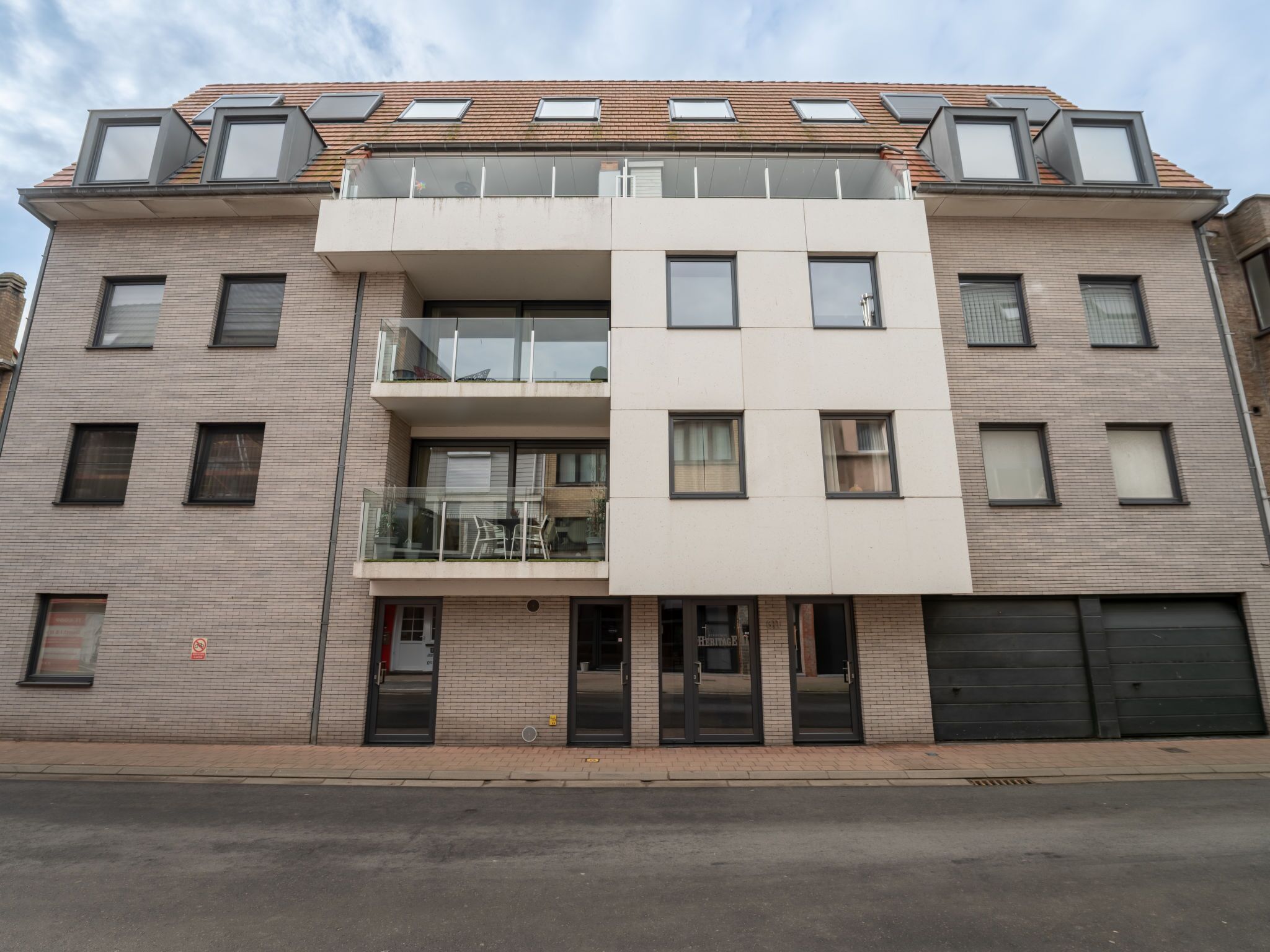 En modern byggnad med flera våningar, ett platt tak, stora fönster och en central balkong.
