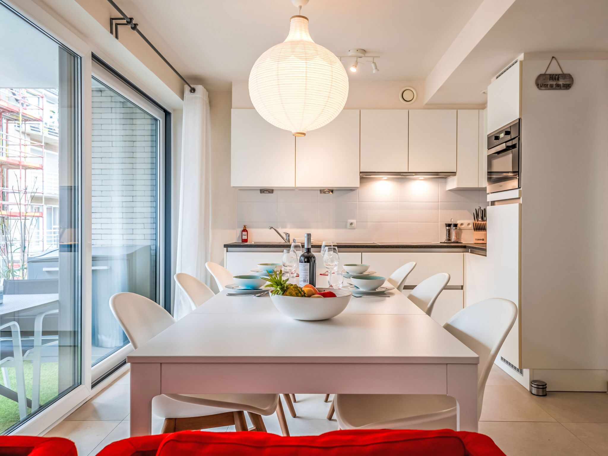 A modern kitchen with white cabinetry, a dining table set for four, and a large window providing a view of the outside.