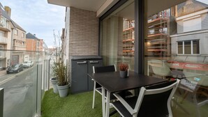 A balcony with a table and chairs, a potted plant, and a view of a street and buildings. - Heritage with parking by Interhome (Bredene)