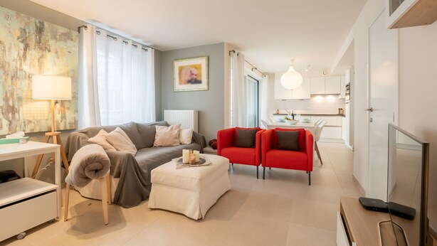 A modern living room with a sofa, ottoman, and red chairs. A dining area with a table and chairs is visible in the background. - Heritage with parking by Interhome (Bredene)