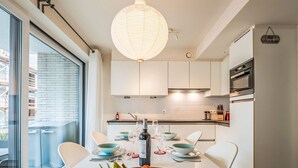 A modern kitchen with white cabinets, a dining table set with plates, glasses, and a bowl of fruit. - Heritage with parking by Interhome (Bredene)