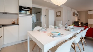 A modern kitchen with white cabinetry, a built-in oven, and a dining area with a white table set for four. - Heritage with parking by Interhome (Bredene)