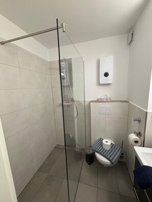 A small bathroom with a glass shower enclosure, a toilet, a sink, and a hand dryer. - In 2nd row to the beach, the sea just a stone's throw away - Gmelinstraße 8 (Wyk auf Föhr)