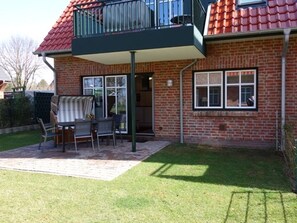 Une maison à deux étages avec une façade en briques, un balcon doté d’une rambarde en métal et un patio aménagé avec du mobilier d  ’extérieur.