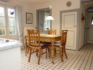 Un comedor con una mesa y sillas de madera, una lámpara colgante y piso de baldosas.