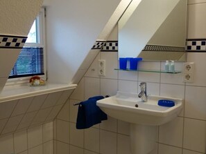 Un baño con lavamanos blanco, un espejo y una ventana con persianas.