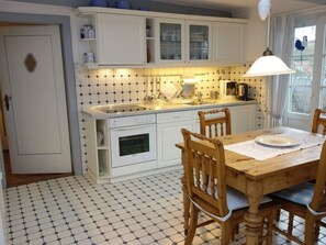 A kitchen with white cabinets, a tiled backsplash, a wooden dining table with chairs, and a window with curtains.