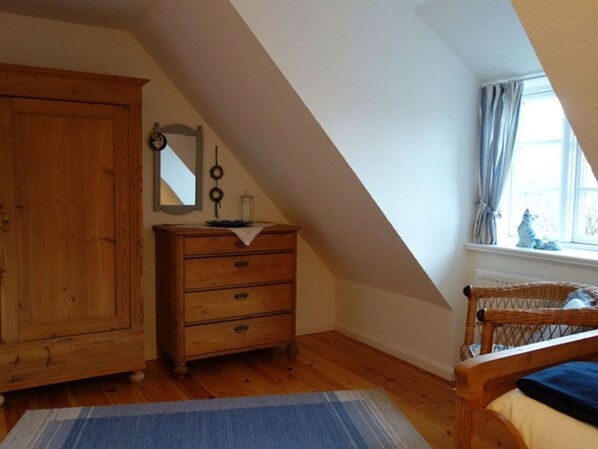 A bedroom with a wooden wardrobe, a dresser, a mirror, and a window with curtains.
