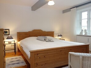 A bedroom with a wooden bed, two bedside lamps, a window with curtains, and a wicker chair.