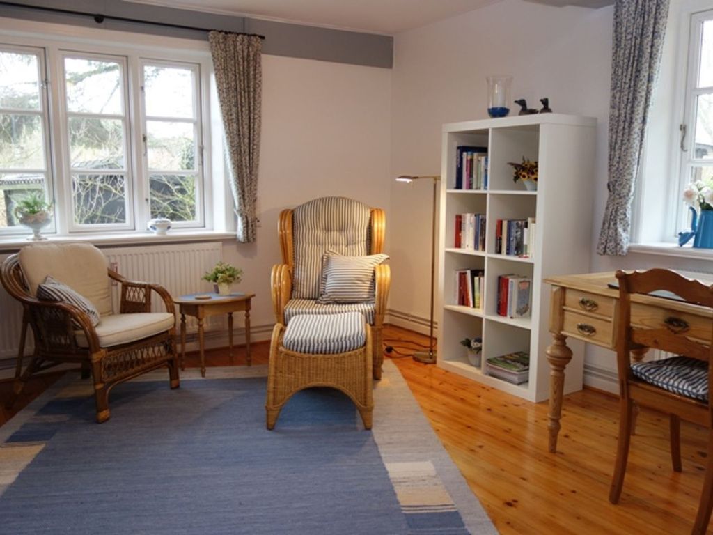 A cozy room with a large window, a bookshelf, a wicker chair, and a wooden desk.