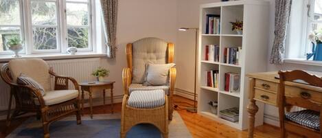 A cozy room with a large window, a bookshelf, a wicker chair, and a wooden desk.