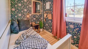 A cozy room with floral wallpaper, a bed with patterned bedding, a small table with a plant, and a window with curtains. - 1 bedroom awesome home in Klövedal (Klövedal)