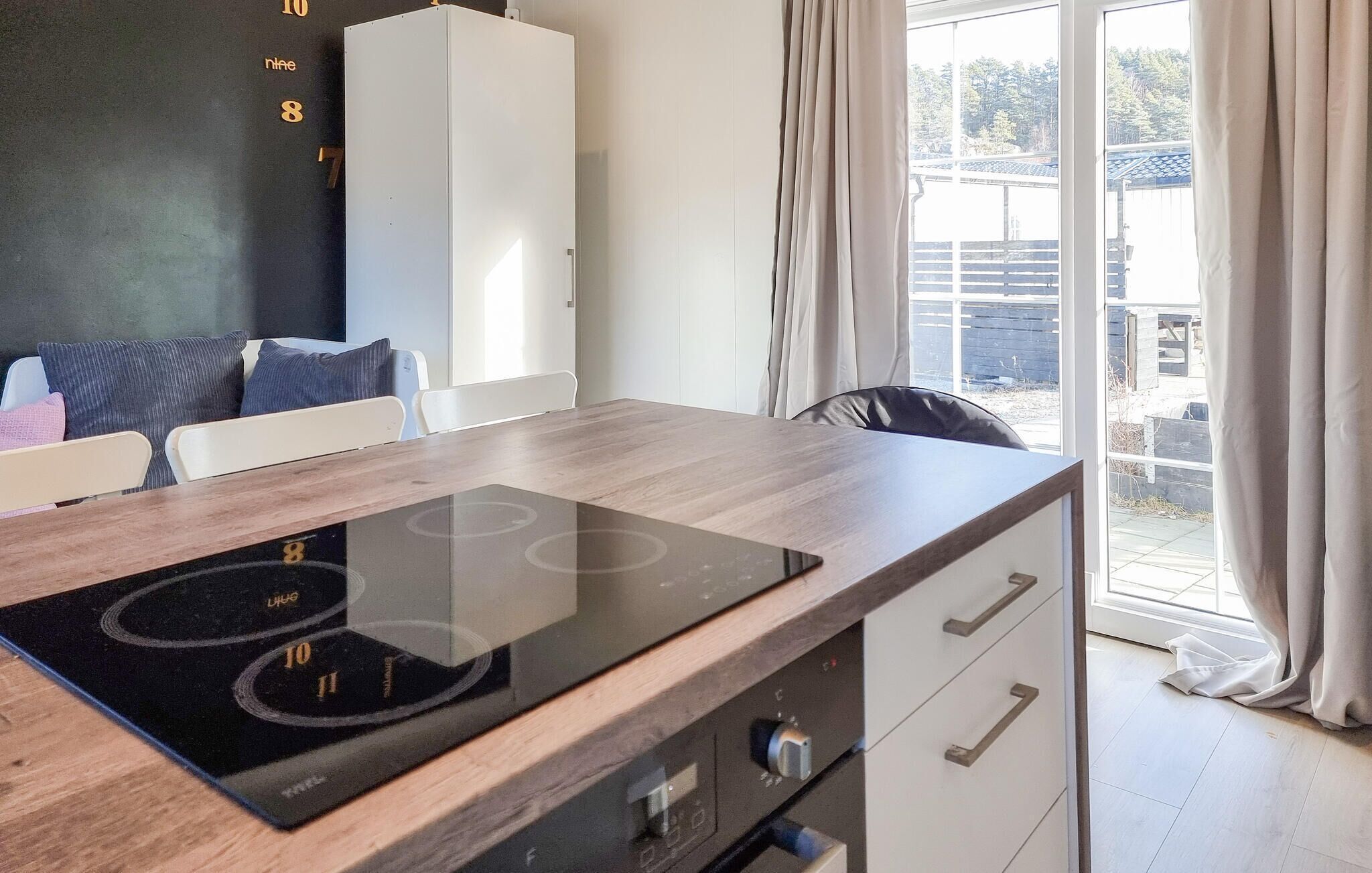 Une cuisine moderne dotée d’une plaque de cuisson à induction intégrée, d’un meuble blanc et offrant une vue sur l’extérieur grâce à de grandes fenêtres.
