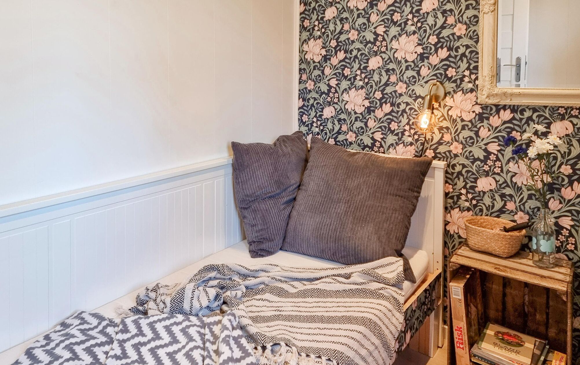 Een kleine, knusse slaapkamer met een enkel bed, een geborreld deken, een bedlamp en bloemenbehang.