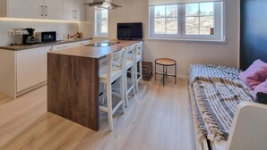 A modern kitchen with white cabinets, a wooden island, and a built-in stove. There is a small dining area with white chairs and a round table. A large window provides a view of the outdoors. - 1 bedroom awesome home in Klövedal (Klövedal)