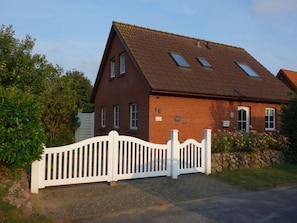 Ett hus byggt av rött tegel med ett vitt staket, en stenmur och en asfalterad uppfart.