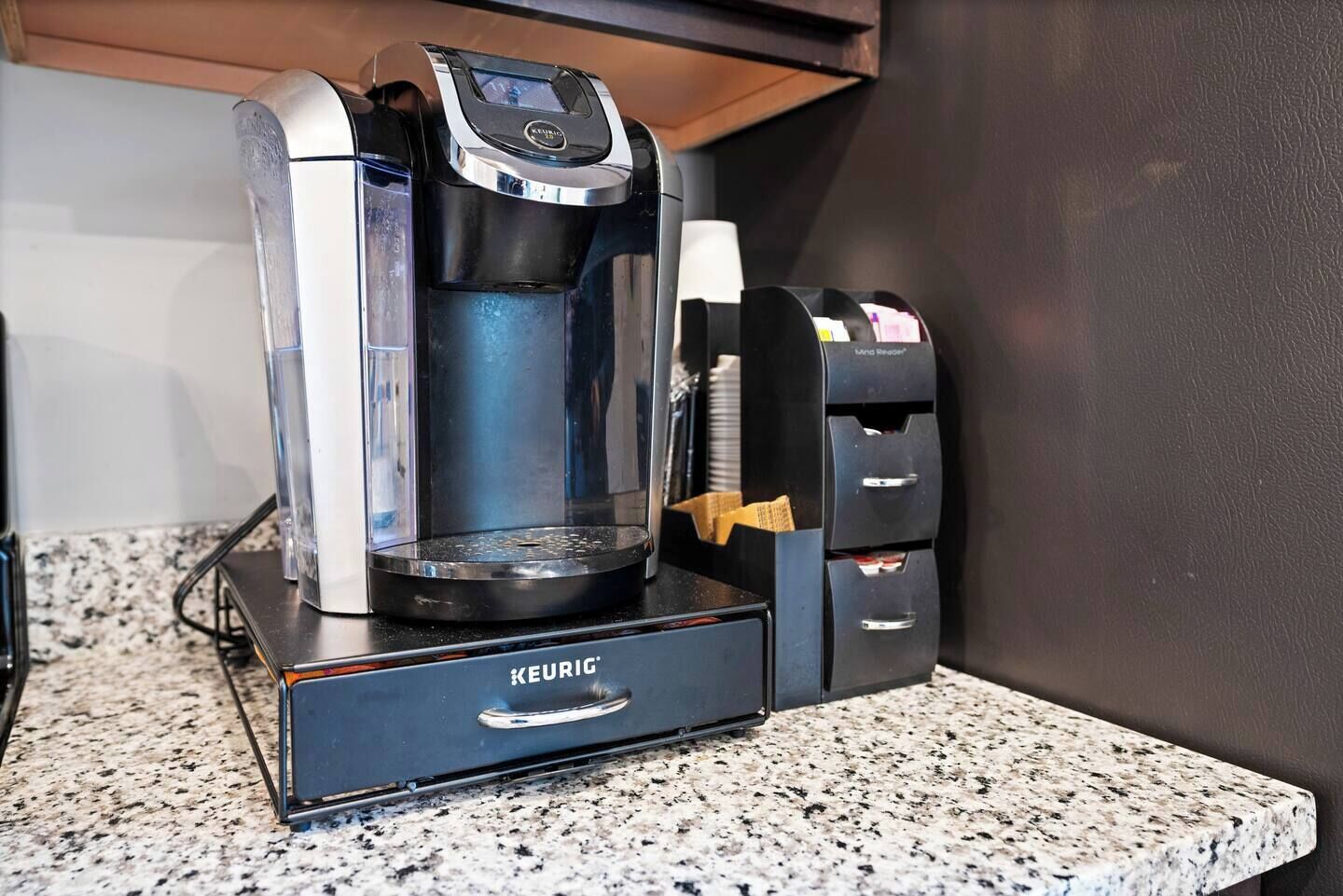 Una cafetera Keurig con un recipiente de goteo y un soporte para cápsulas sobre una encimera de granito.