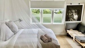A bedroom with a bed, a window with a view, a sofa, and a painting. - Beach side home + Separate apartment Raumati South (Paraparaumu)