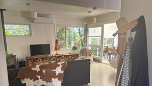 A modern living room with a large TV, a fireplace, and a view of the outdoors. - Beach side home + Separate apartment Raumati South (Paraparaumu)