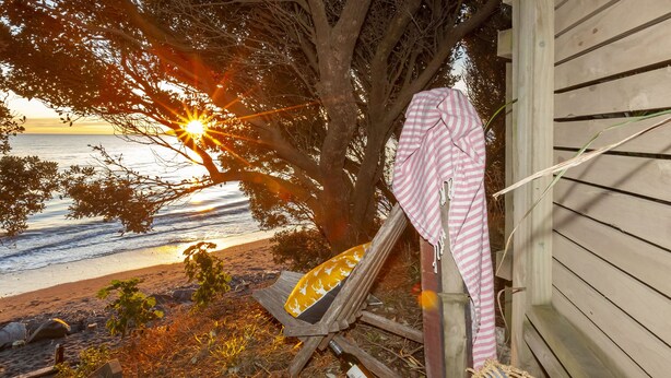 A beach view with a wooden structure, a chair, and a blanket. - Beach side home + Separate apartment Raumati South (Paraparaumu)