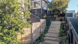 A modern house with a wooden staircase leading to a deck area, surrounded by lush greenery and a garage. - Beach side home + Separate apartment Raumati South (Paraparaumu)