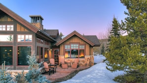 A two-story house with a stone exterior, large windows, and a patio area with outdoor seating. - Long Ridge Lodge | Heavenly Views and Private Spa, Quiet Neighborhood. (Breckenridge)