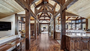 A spacious hall with wooden beams, a stone fireplace, and a large kitchen area with wooden cabinets. - Long Ridge Lodge | Heavenly Views and Private Spa, Quiet Neighborhood. (Breckenridge)