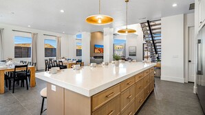 A modern kitchen with a large island, wooden cabinets, and pendant lighting.