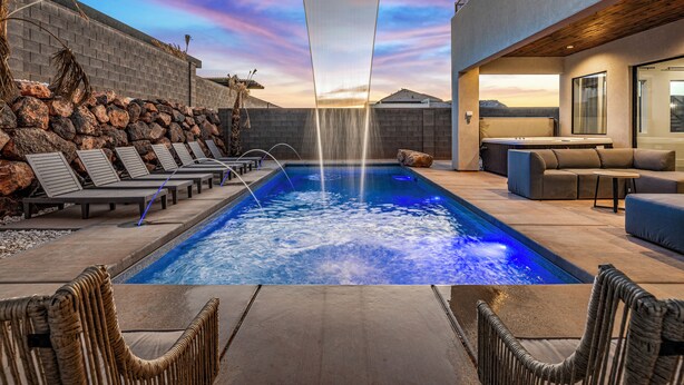 A swimming pool with lounge chairs and a hot tub, surrounded by a stone wall and wooden beams.