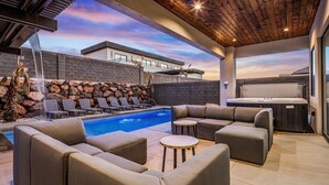 An outdoor pool area with a modern design, including a stone wall, lounge chairs, and a hot tub.