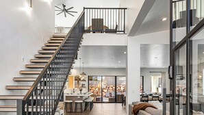 A spacious interior with a staircase leading to a second floor, a dining area with a stone wall backdrop, and a seating area with a sofa and cushions.