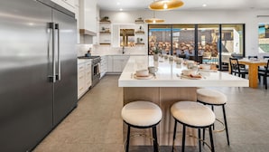 A modern kitchen with a large island, stainless steel appliances, and a view of a stone wall and outdoor seating area.