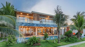 Een modern herenhuis met twee verdiepingen, een glazen gevel, een zwembad en een keurig onderhouden tuin met palmbomen.