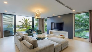 Een moderne woonkamer met een ruime bank, een salontafel en een flatscreen-televisie aan de muur. Er is een balkon met uitzicht op palmbomen.