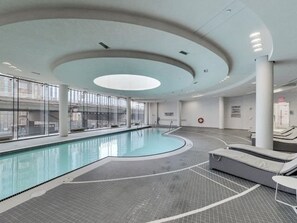 An indoor swimming pool with a curved design, large windows, and a modern ceiling. - Beautiful Luxurious Modern Suite (Toronto)