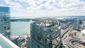 A modern high-rise building with a glass facade, surrounded by a cityscape and a body of water.
