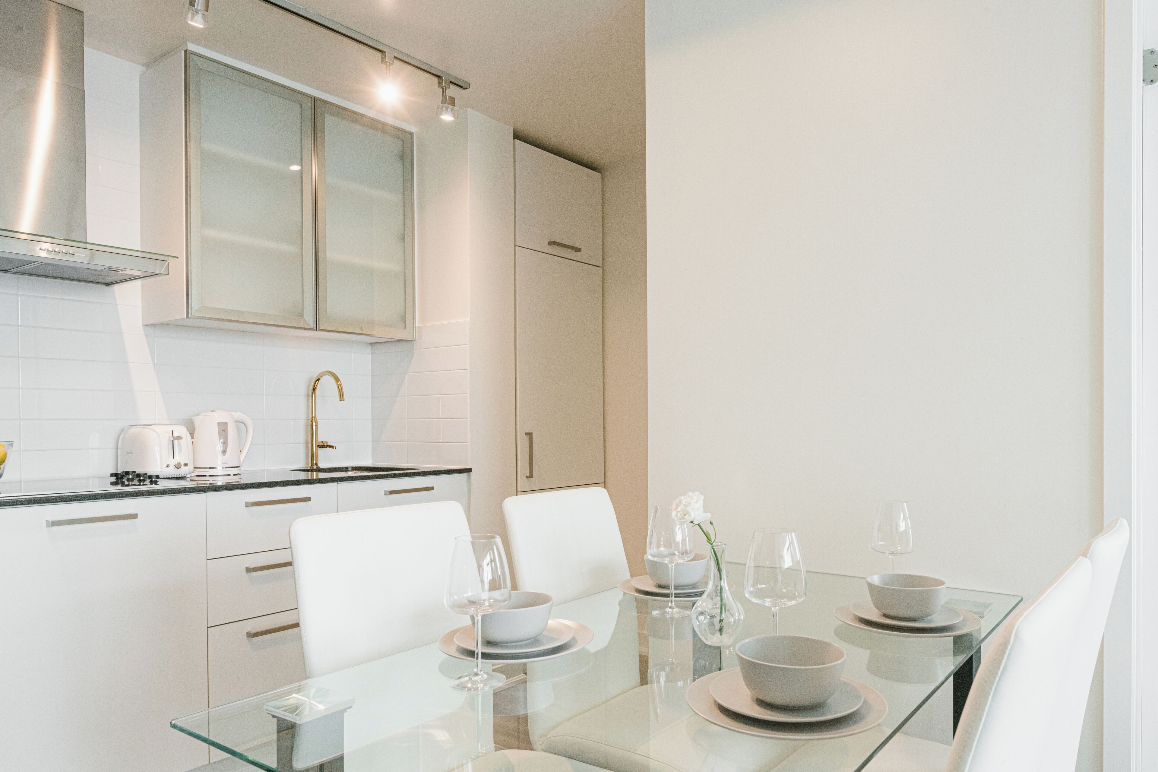 A modern kitchen with white cabinetry, a glass dining table set with bowls, plates, and wine glasses.