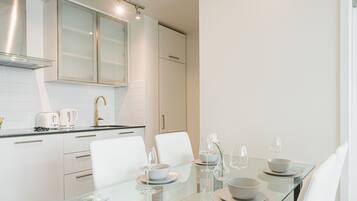 A modern kitchen with white cabinetry, a glass dining table set with bowls, plates, and wine glasses.