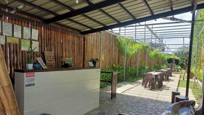 A reception area with a bamboo wall, a reception desk, and a covered outdoor seating area with tables and chairs. - BC Lodge (Puerto Princesa)