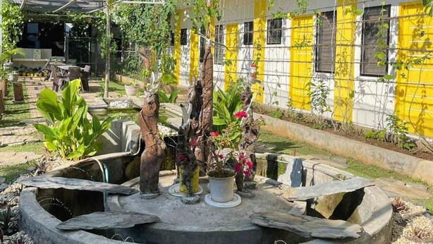 A courtyard with a fountain, potted plants, and a building with yellow and white walls. - BC Lodge (Puerto Princesa)