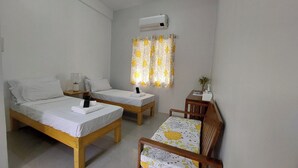A small, clean room with two single beds, a wooden chair, a small table, and a window with curtains. - BC Lodge (Puerto Princesa)