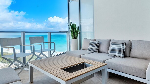 Ein Balkon mit Blick auf den Ozean, eine Couch, ein Couchtisch und ein Blumentopf.