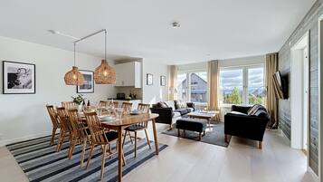 Ett modernt vardagsrum med matplats, stora fönster och en platt-TV.