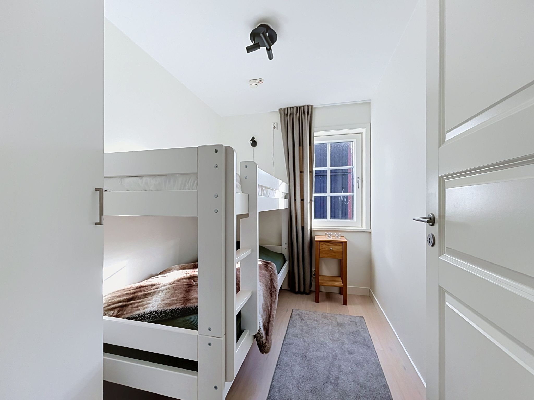 A room with bunk beds, a desk, a chair, and a window with curtains.